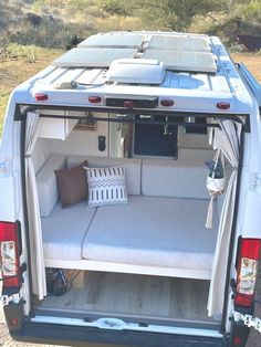 the back end of a white van with its doors open and two pillows on it