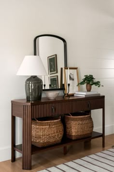 a table with two baskets under a mirror and a lamp next to it on top of a hard wood floor