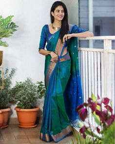 a woman in a blue and green sari standing on a balcony next to potted plants