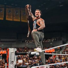 a man standing on top of a wrestling ring holding a belt in the air with his right hand