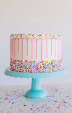 a birthday cake with sprinkles and frosting on a blue pedestal surrounded by confetti