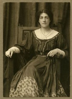 an old black and white photo of a woman in a dress sitting on a chair