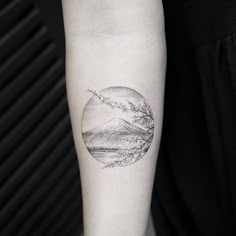 a woman's arm with a tattoo on it that has mountains and trees in the background