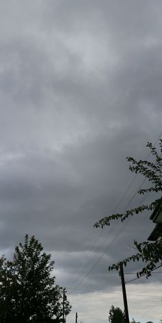 the sky is dark and cloudy with some trees in front of it on an overcast day