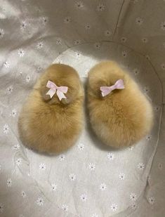 a pair of furry slippers with pink bows on the front and back, sitting on a white bed sheet