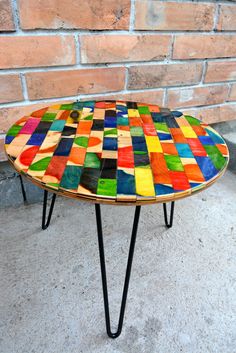 a multicolored table sitting on top of a cement floor next to a brick wall