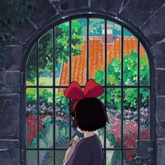 a girl looking out an iron window at the garden outside her house, with a red bow on her head