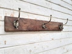 a wooden coat rack with two hooks on the side of a white building next to a brick wall