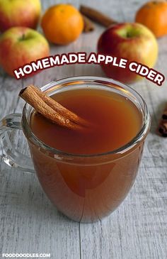 a cup of apple cider with cinnamon and apples in the background