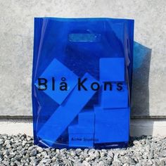 a blue plastic bag with black letters on it sitting next to a stone wall and gravel