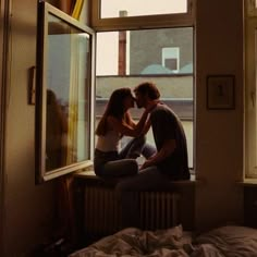 two people sitting on a window sill in front of a window and one person kissing the other