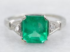 an emerald and diamond ring on a white surface with diamonds around the band, set in 18k white gold