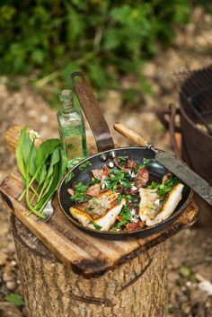 a frying pan filled with fish and vegetables next to a bbq grill on top of a tree stump