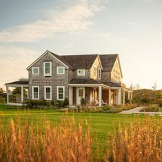 a large gray house sitting on top of a lush green field next to tall grass