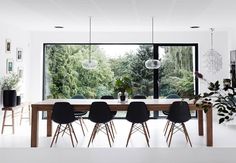 a dining room table with black chairs and a large window overlooking the trees in the distance