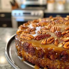 a cake with pecans on top sitting on a metal platter in front of a stove