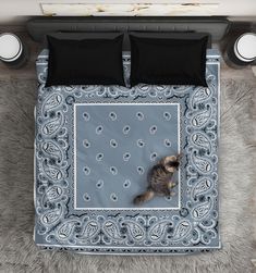 a cat laying on top of a bed covered in grey blankets and pillows with black trim