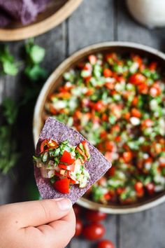 someone holding up a tortilla chip with salsa in the background