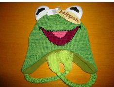 a green knitted hat with a smiling frog on it's face and eyes