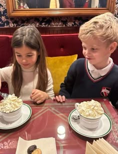 two children sitting at a table eating desserts