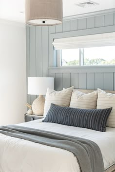 a bed with white sheets and pillows in a bedroom next to a window that has blue paneling on the walls