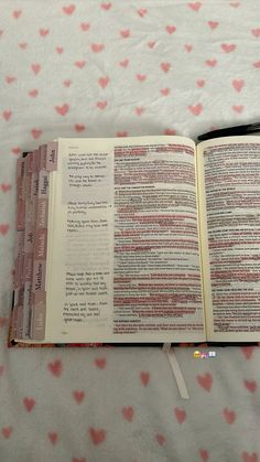 an open bible on a bed with pink hearts