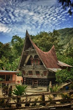 an old wooden house in the middle of some trees and bushes with mountains in the background