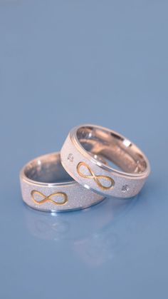 two wedding rings sitting on top of a blue surface with gold lettering in the middle