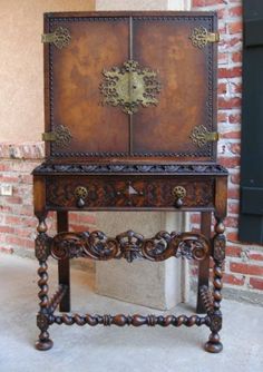 an old wooden cabinet with ornate carvings on the top and bottom, sitting in front of a brick wall