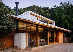 a modern house with an outdoor kitchen and living area in the middle of it, surrounded by trees