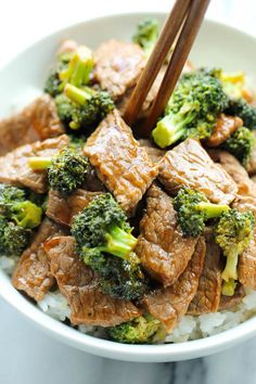 beef and broccoli stir fry in a white bowl with chop sticks sticking out of it