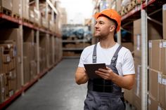 a man in an orange hard hat is looking up at something on his clipboard