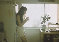 a woman standing in front of a window next to a potted plant on a counter