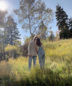 two people standing in tall grass with trees in the background and sun shining on them