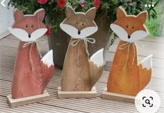 four wooden foxes sitting next to each other in front of potted plants and flowers