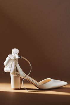 a pair of white high heeled shoes with bows on the toes and heels are shown in front of a brown background