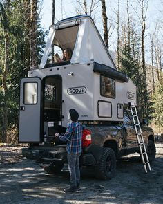 a man standing in the back of a truck next to a white camper trailer