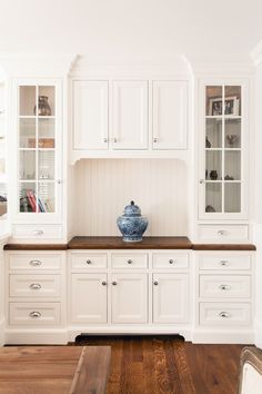 a white kitchen with wooden floors and cabinets in the corner, along with a blue vase on the countertop