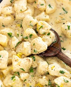 a wooden spoon in a bowl filled with dumplings and cheese sauce on the side