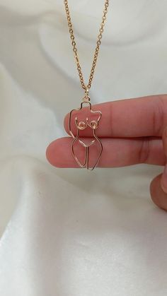 a hand holding a gold necklace with a small cat on it's face in the shape of a heart