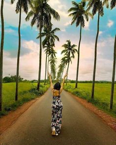 a woman standing in the middle of an empty road with palm trees on both sides