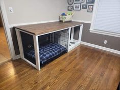 a dog crate with a bed in it on top of a hard wood floor next to a window