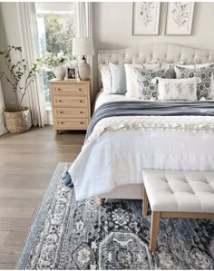 a white bed with blue and gray pillows on top of it next to a window