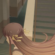 a girl with long hair standing in front of stairs and looking down at the ground