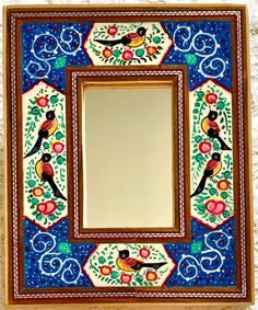 a decorative mirror with birds and flowers painted on the frame, hanging on a wall