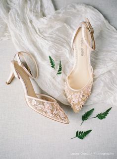 two pairs of shoes sitting on top of a white blanket next to green plant leaves