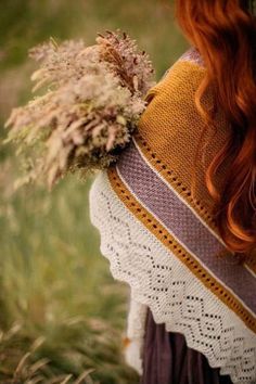 a woman with red hair wearing a knitted sweater and holding a dried flower in her hand