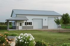 a white barn with flowers in the foreground and grass on the ground next to it