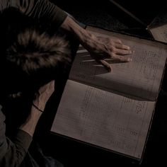 a man sitting at a table with an open book in front of him and his hand on top of it