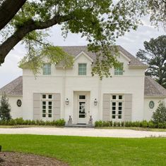 a large white house sitting on top of a lush green field next to a tree